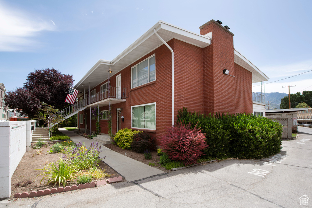 View of property exterior with brick siding, a chimney, and stairway