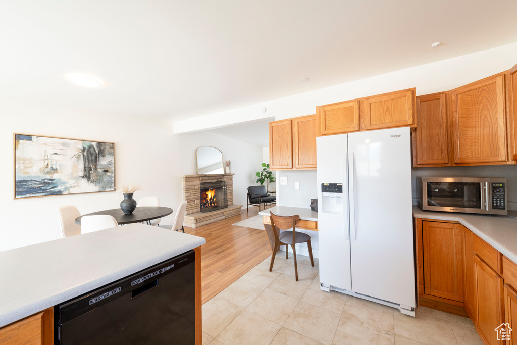 Kitchen with white refrigerator with ice dispenser, dishwasher, stainless steel microwave, light countertops, and a stone fireplace