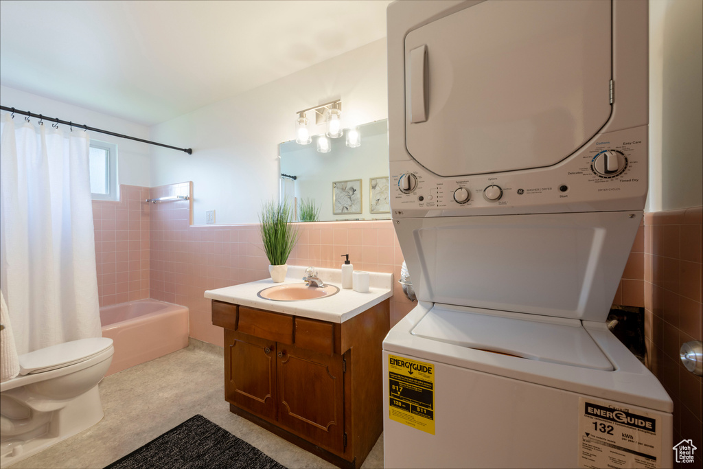 Bathroom with stacked washing machine and dryer, tile walls, vanity, shower / bath combination with curtain, and wainscoting