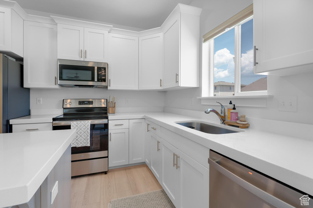 Kitchen with stainless steel appliances, white cabinetry, light countertops, and light wood-style flooring