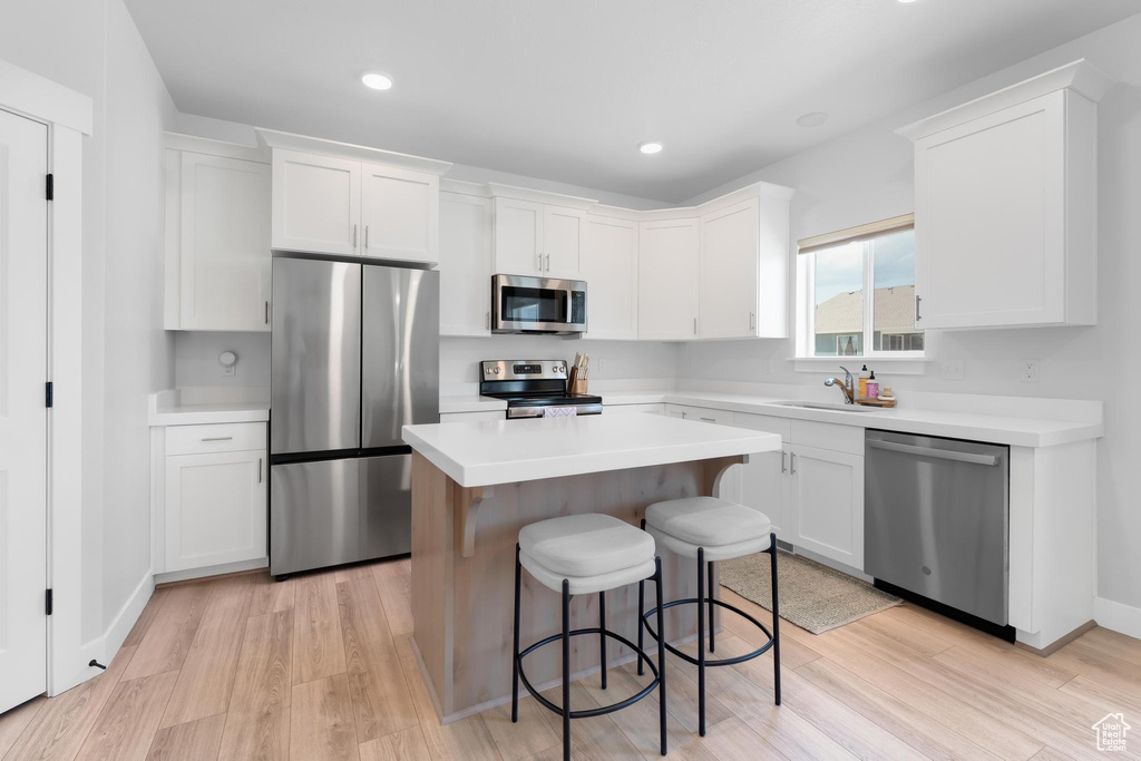 Kitchen featuring stainless steel appliances, light wood-style floors, a kitchen bar, white cabinetry, and a kitchen island
