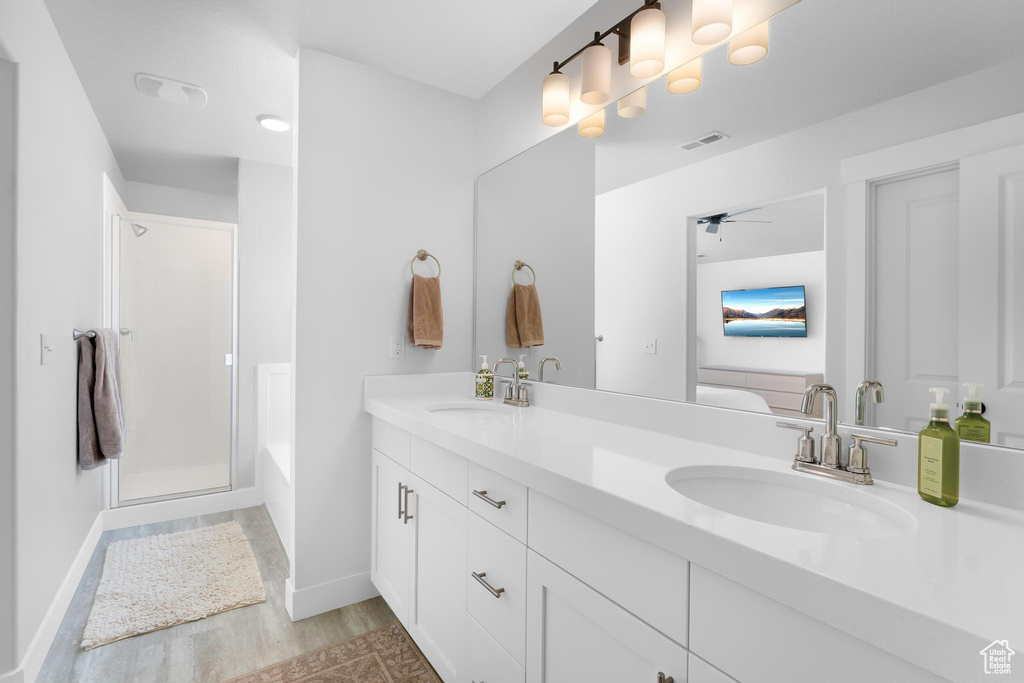 Full bathroom featuring double vanity, wood finished floors, a bath, a shower with shower door, and ceiling fan