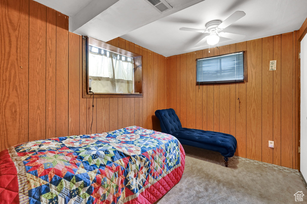 Bedroom featuring carpet, wood walls, and a ceiling fan