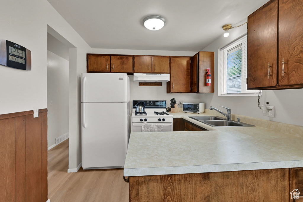 Kitchen featuring white appliances, under cabinet range hood, light countertops, light wood-style floors, and a peninsula