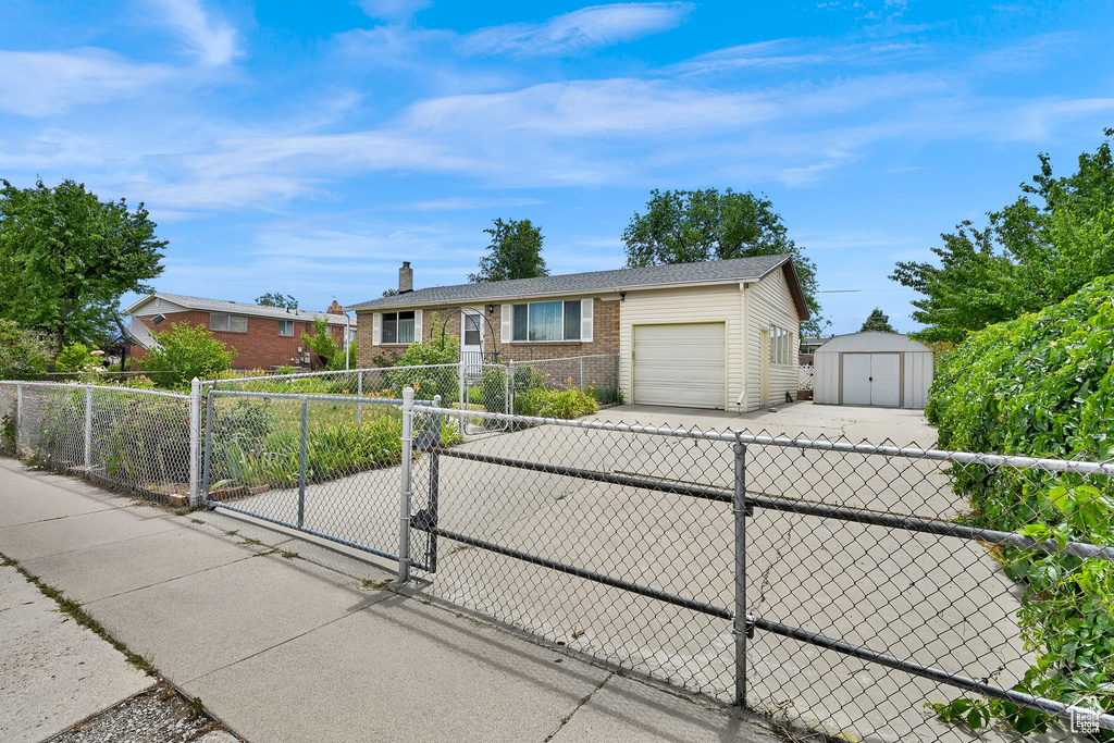Single story home with a storage unit, brick siding, a garage, driveway, and a chimney