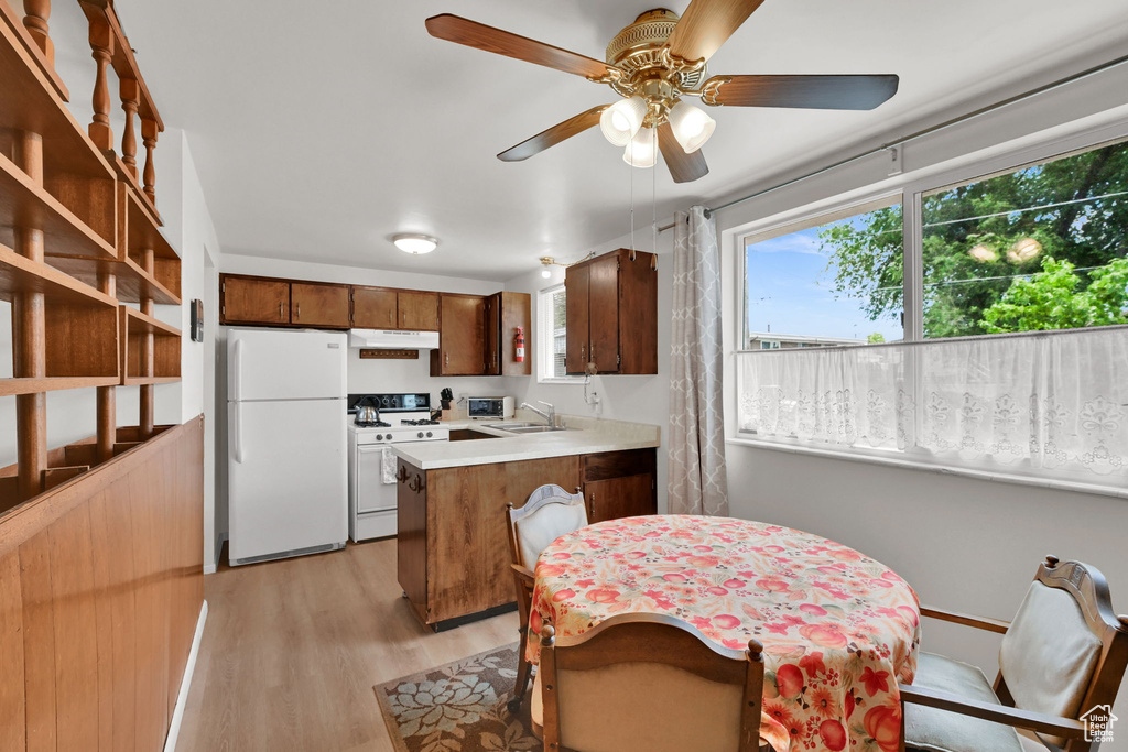 Kitchen with white appliances, light wood-style floors, a peninsula, under cabinet range hood, and ceiling fan
