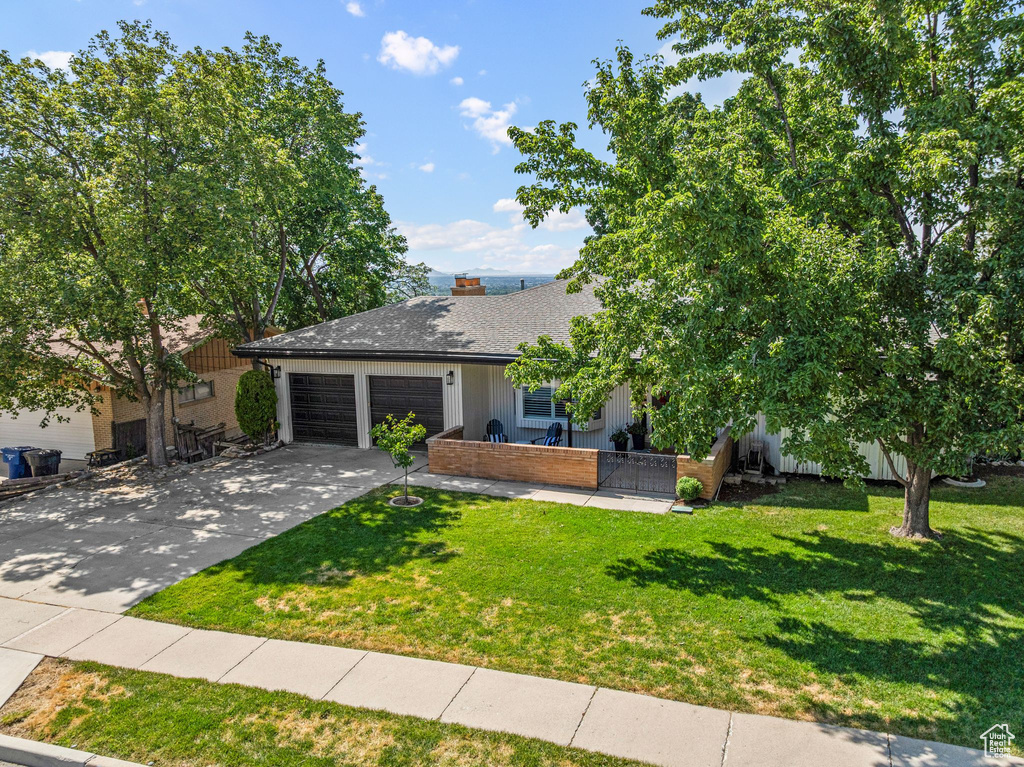 View of front of home with an attached garage, a front lawn, concrete driveway, and a chimney