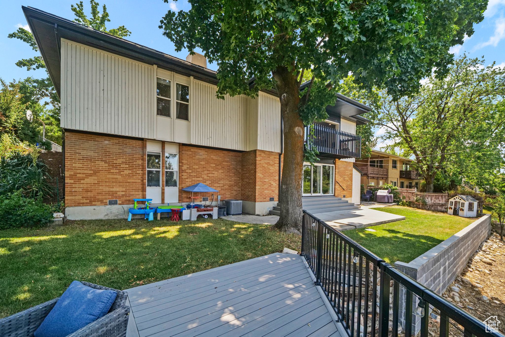 Back of house with brick siding, a balcony, a yard, and a chimney