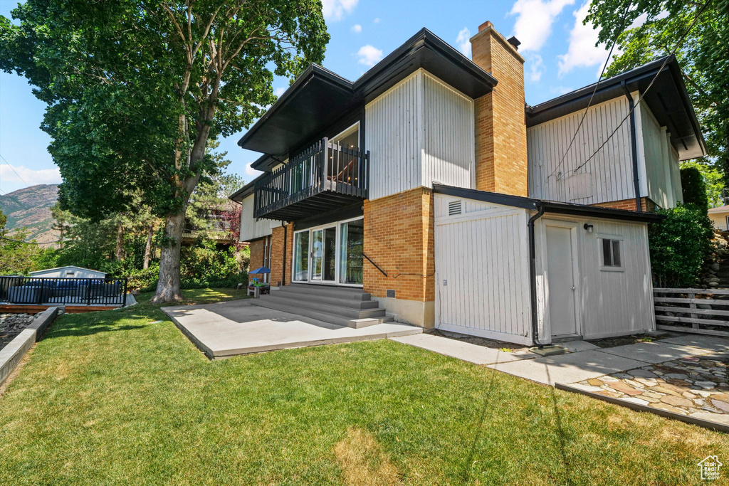 Rear view of house featuring a balcony, a chimney, brick siding, a patio area, and entry steps