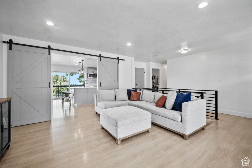 Living room with a barn door, light wood-style flooring, and recessed lighting