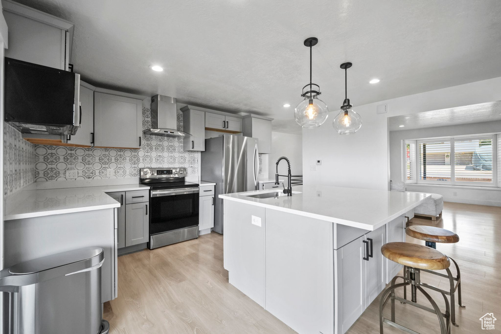 Kitchen with stainless steel appliances, wall chimney exhaust hood, gray cabinets, light wood finished floors, and light countertops