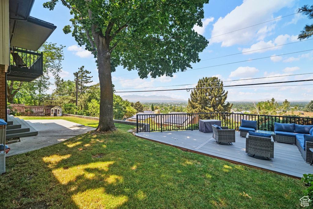 View of green lawn with an outdoor living space, a deck, and a shed