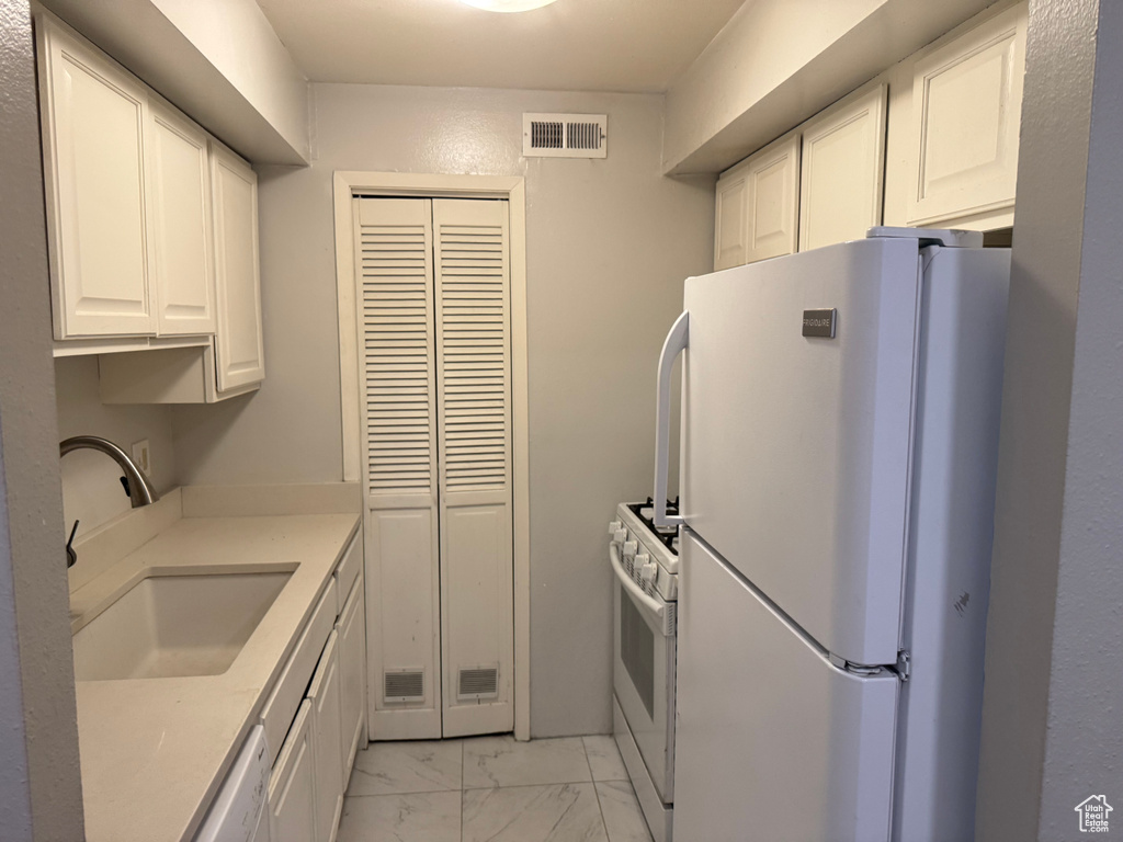Kitchen with white appliances, light marble finish flooring, white cabinetry, and light countertops