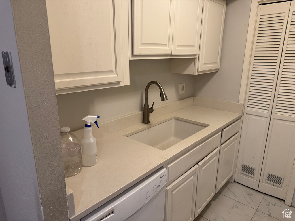 Kitchen featuring dishwasher, light marble finish flooring, and white cabinetry