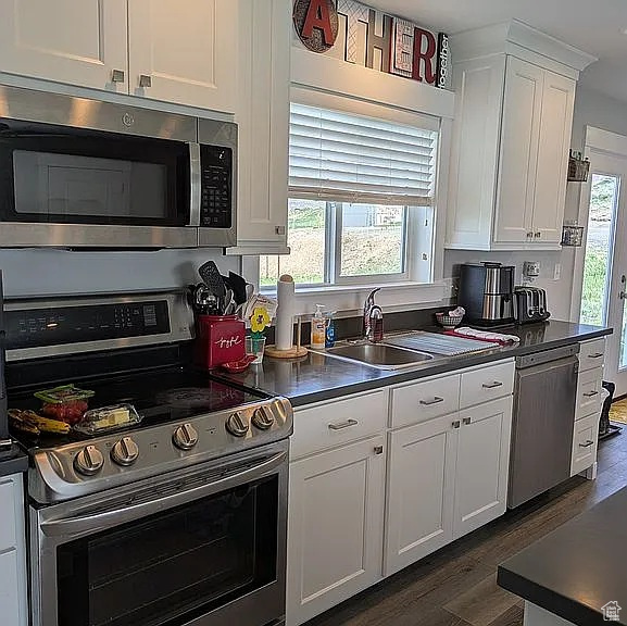 Kitchen with appliances with stainless steel finishes, dark wood finished floors, white cabinets, and dark countertops