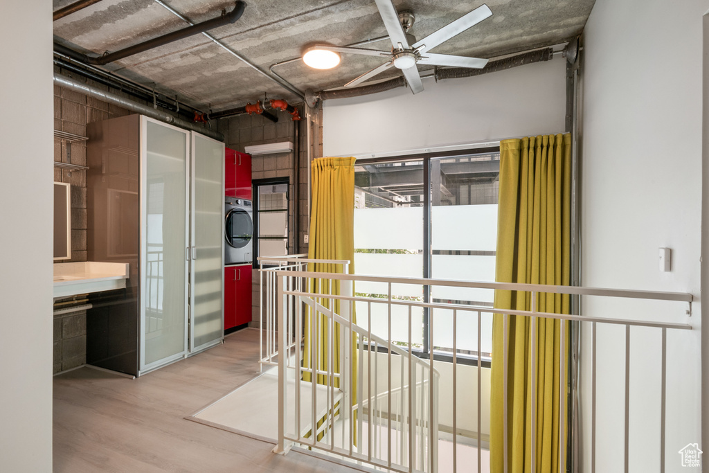 Hall with stacked washer and clothes dryer, wood finished floors, and an upstairs landing