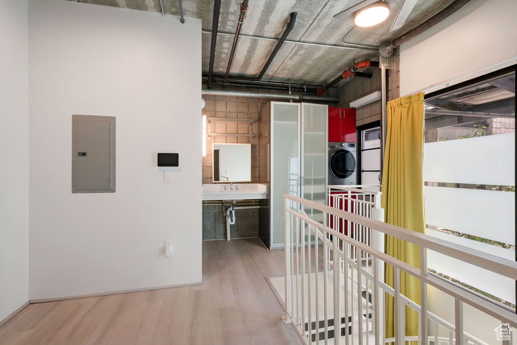 Hallway with electric panel, wood finished floors, and stacked washer and clothes dryer
