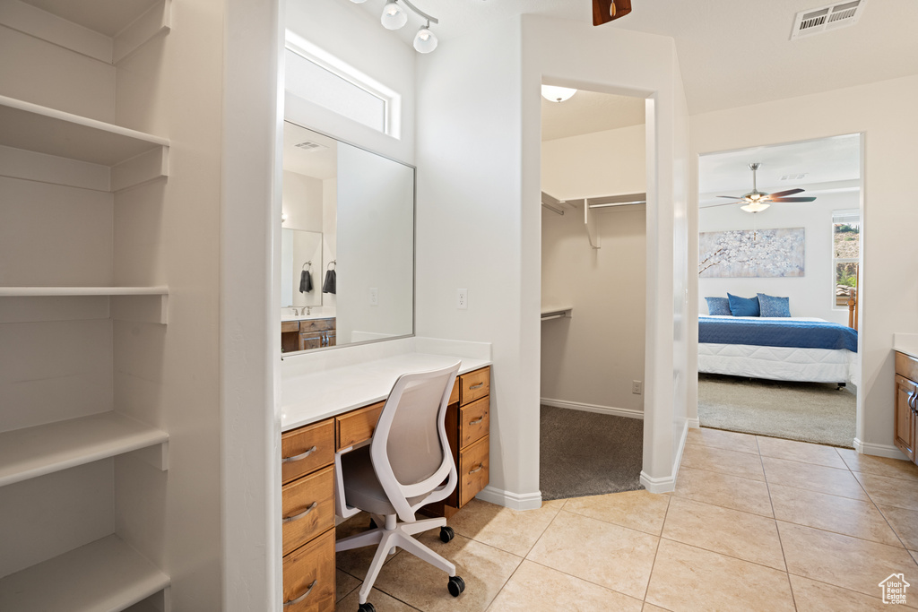Home office featuring built in desk, light carpet, light tile patterned flooring, and a ceiling fan
