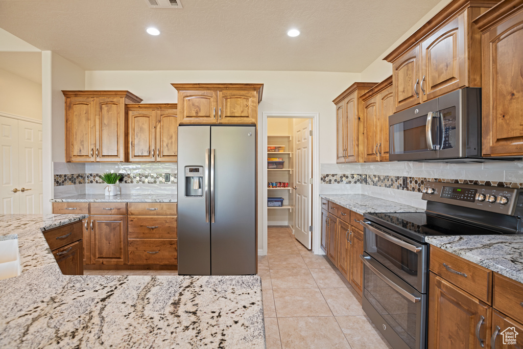 Kitchen with stainless steel appliances, light stone countertops, tasteful backsplash, brown cabinetry, and recessed lighting