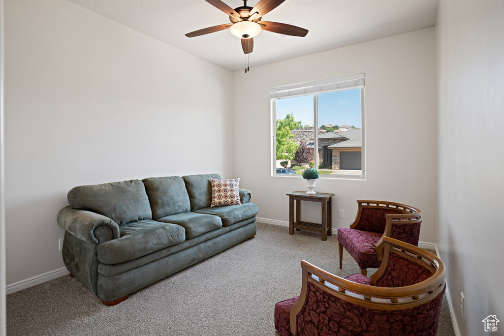 Carpeted living area featuring ceiling fan and baseboards