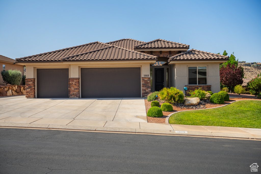Mediterranean / spanish house featuring a garage, stucco siding, driveway, a tile roof, and a front lawn