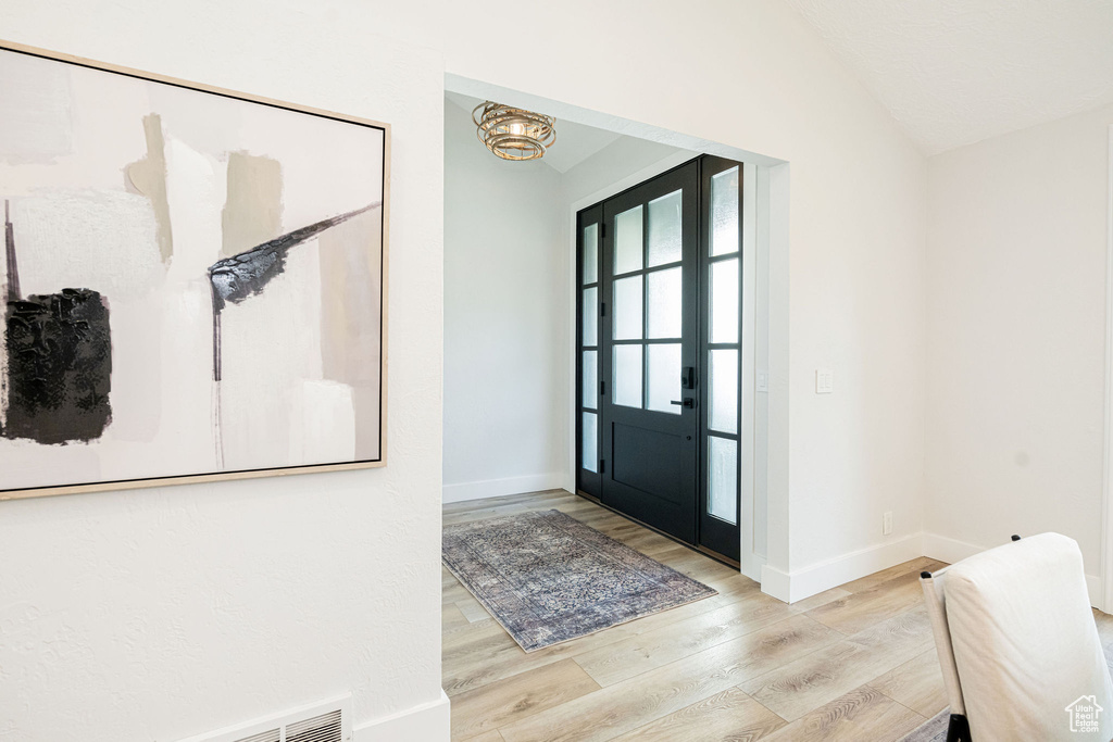 Foyer with wood finished floors, lofted ceiling, and a chandelier