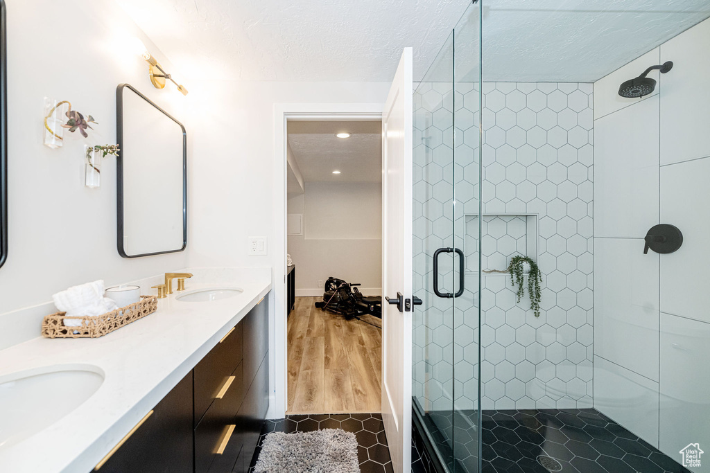 Bathroom featuring a stall shower, double vanity, a textured ceiling, wood finished floors, and recessed lighting
