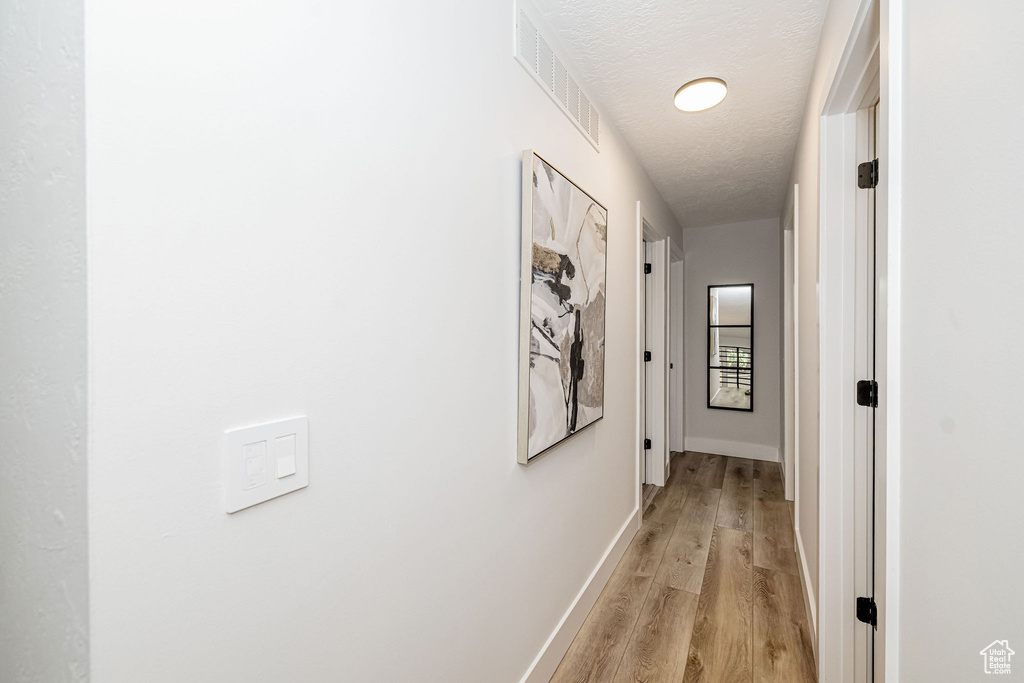 Corridor with light wood finished floors and a textured ceiling
