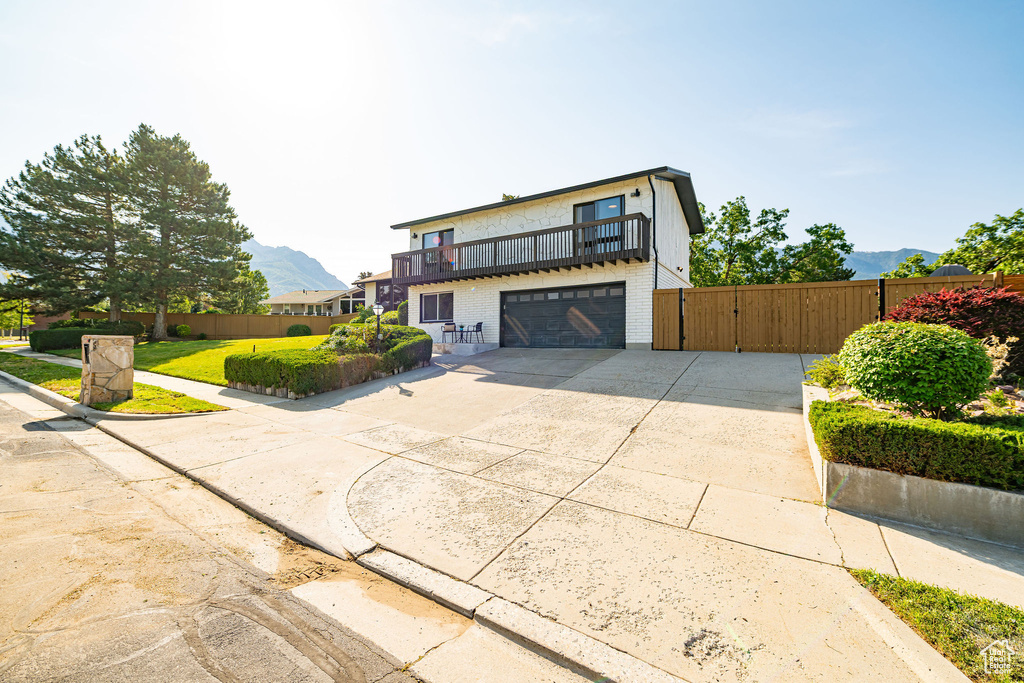View of front of home featuring a balcony, a garage, a gate, concrete driveway, and brick siding