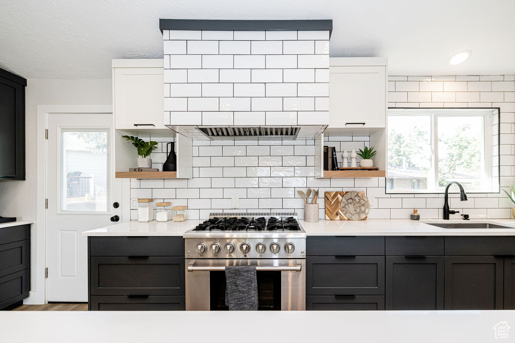 Kitchen featuring stainless steel range, open shelves, light countertops, and backsplash