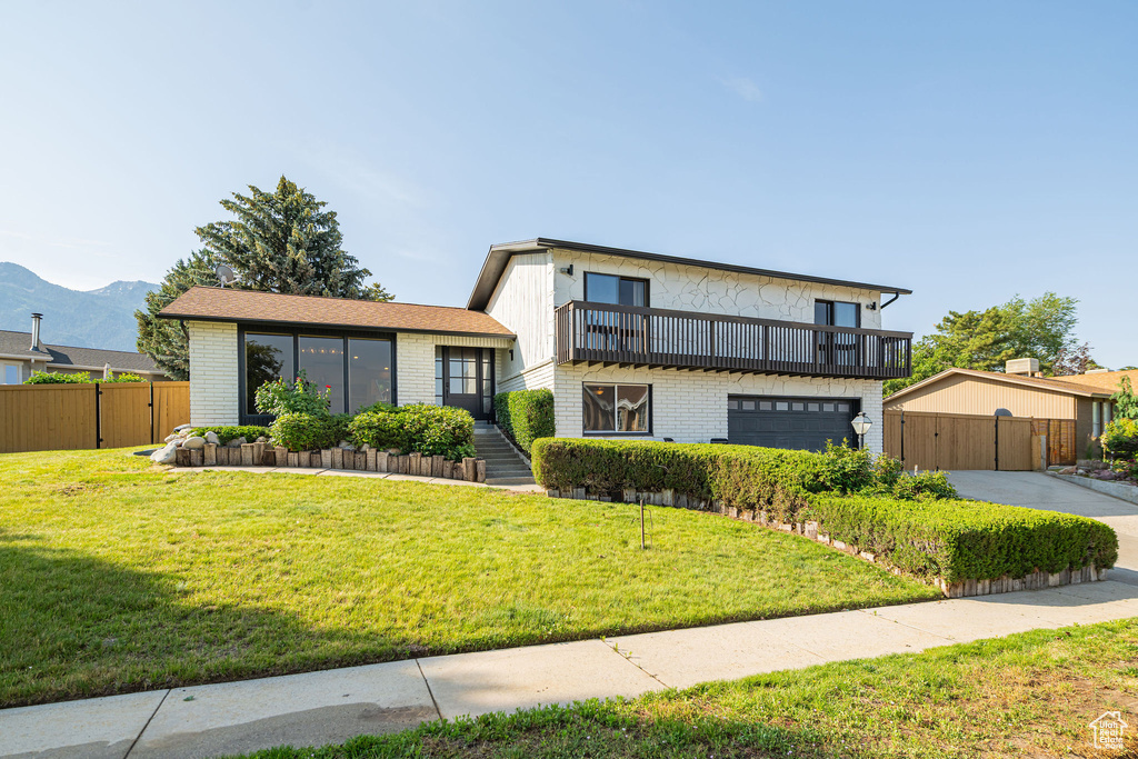 View of front of house with brick siding, a balcony, concrete driveway, a garage, and a mountain view