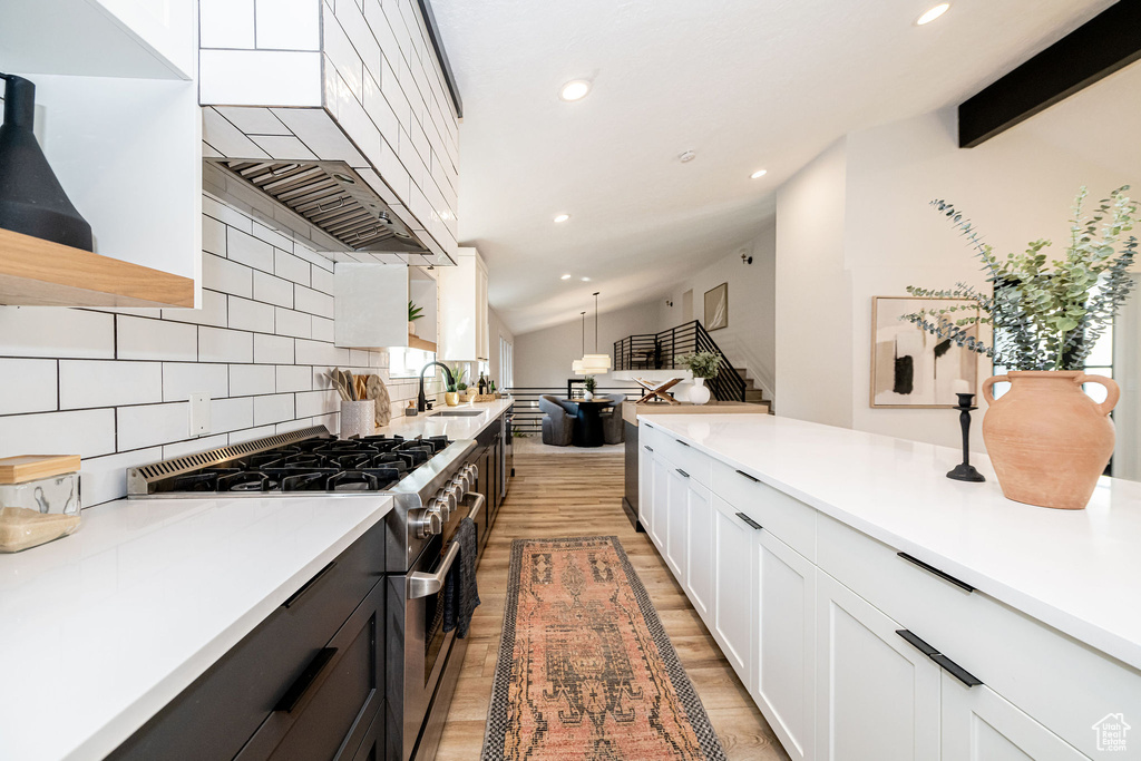Kitchen featuring stainless steel range, backsplash, light countertops, white cabinets, and light wood-style flooring