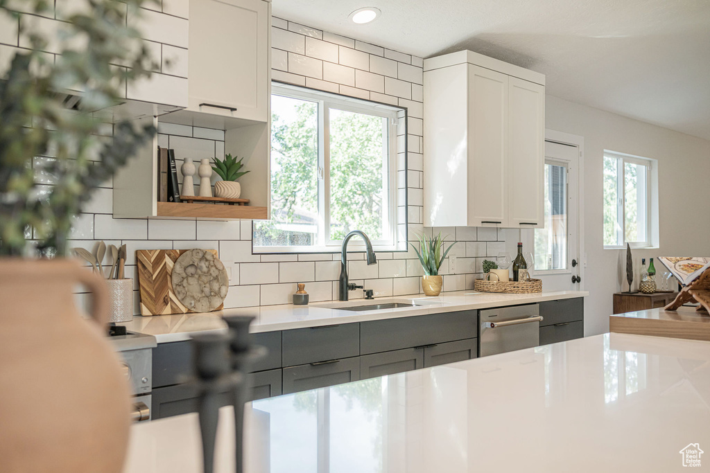 Kitchen featuring gray cabinets, stainless steel dishwasher, light countertops, tasteful backsplash, and white cabinets