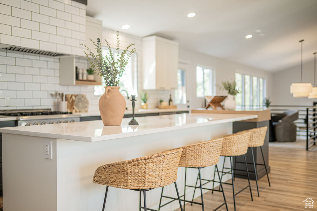 Kitchen featuring tasteful backsplash, light countertops, light wood-type flooring, premium range hood, and recessed lighting