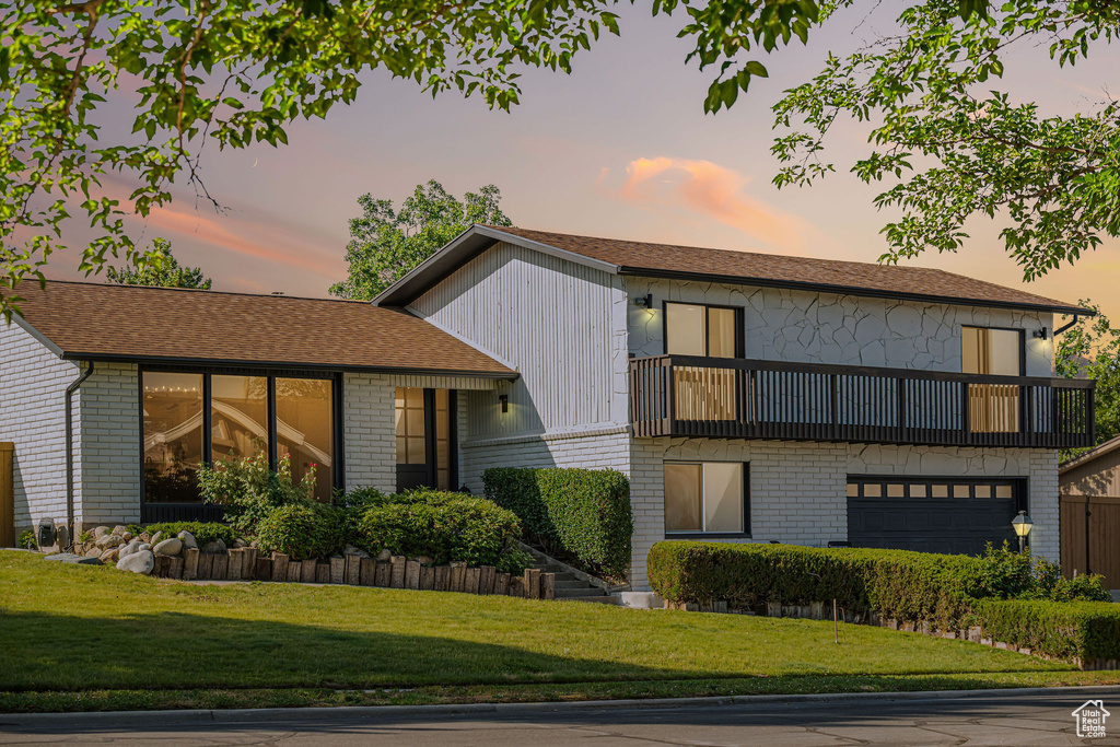 View of front facade with a balcony, a lawn, brick siding, and an attached garage