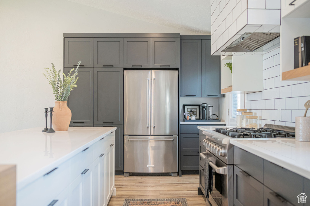 Kitchen with high quality appliances, premium range hood, gray cabinets, light wood-style floors, and tasteful backsplash