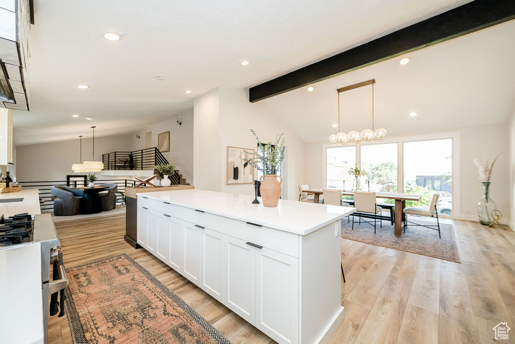Kitchen with white cabinets, a center island, light wood-style floors, stainless steel gas range, and light countertops