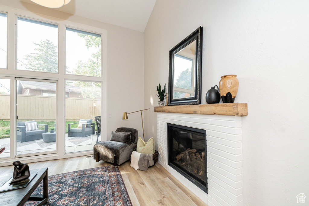 Living room with wood finished floors, a brick fireplace, and lofted ceiling