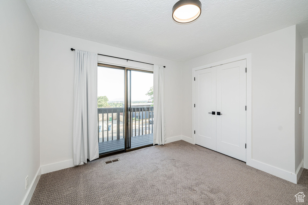 Unfurnished bedroom featuring access to outside, carpet floors, a textured ceiling, and a closet