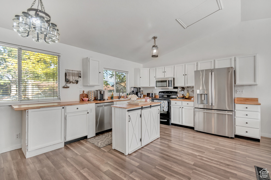 Kitchen featuring appliances with stainless steel finishes, light wood-style floors, white cabinetry, vaulted ceiling, and hanging light fixtures