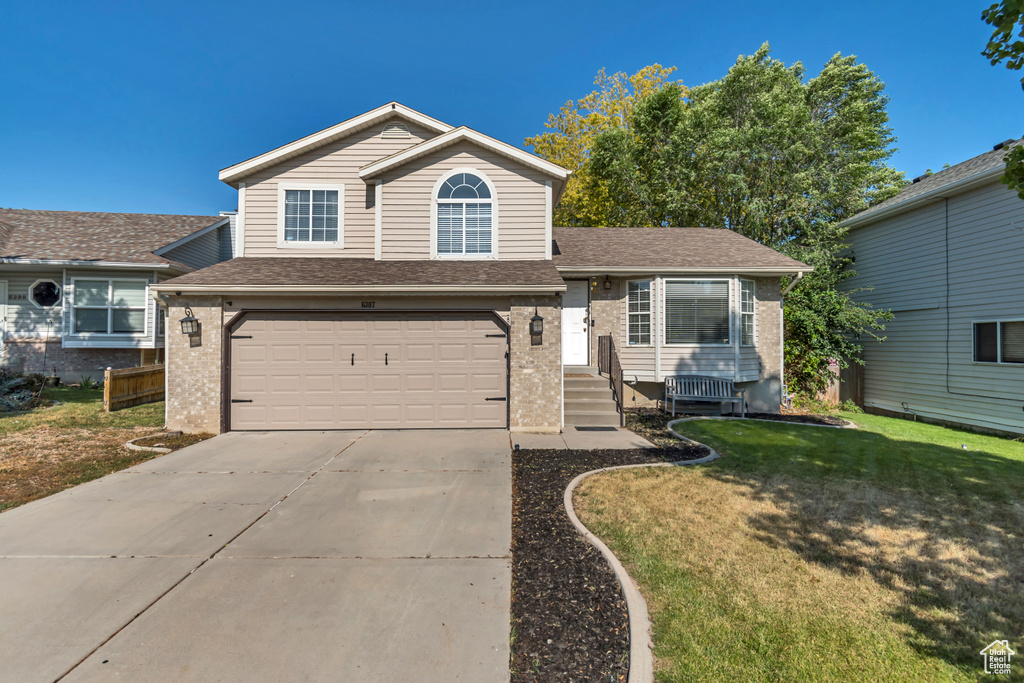 Split level home with brick siding, an attached garage, concrete driveway, a front yard, and roof with shingles