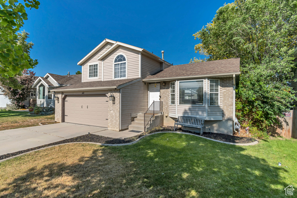 Tri-level home featuring driveway, a front yard, a garage, roof with shingles, and brick siding
