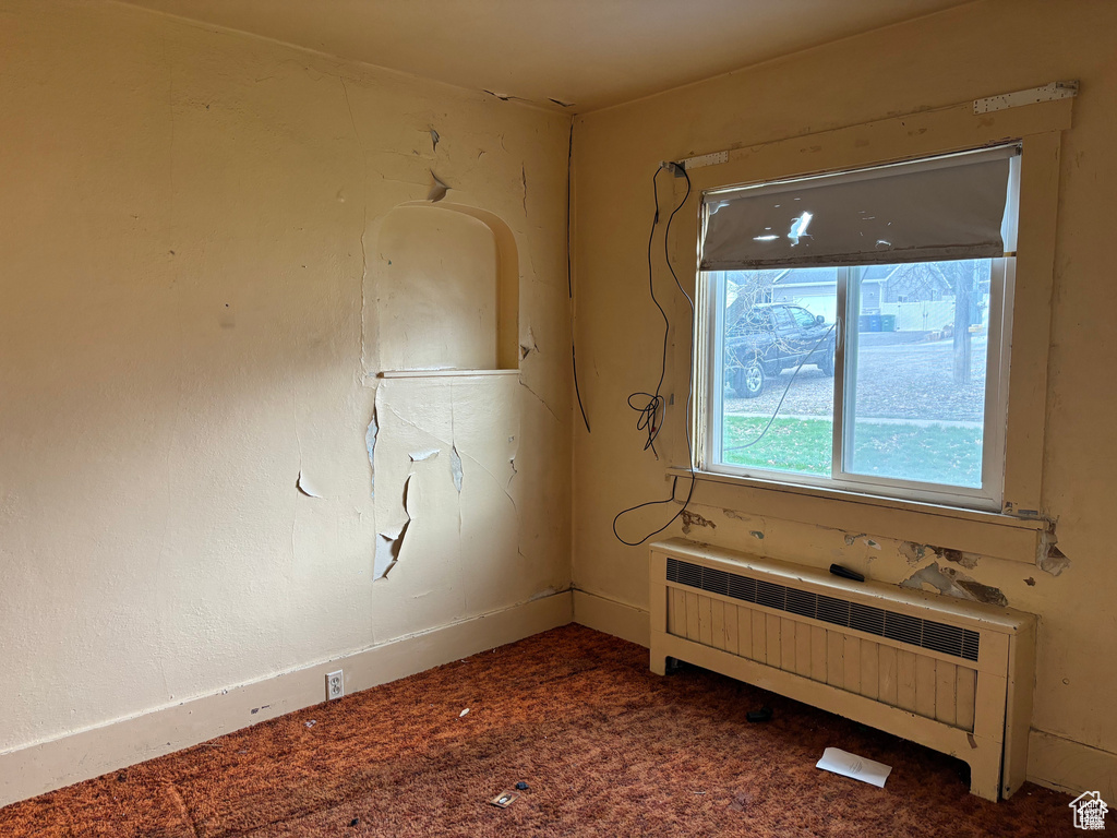 Carpeted empty room featuring radiator heating unit