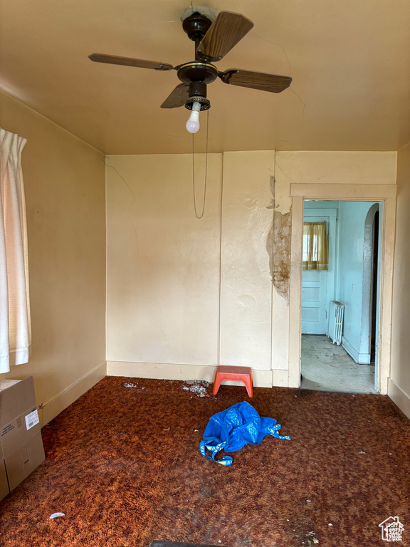 Carpeted empty room featuring ceiling fan and radiator