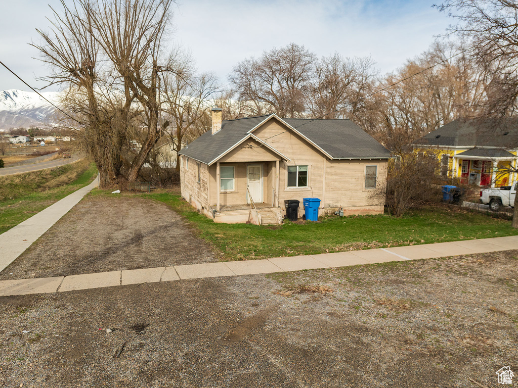 View of front of property featuring a chimney, roof with shingles, and a front yard