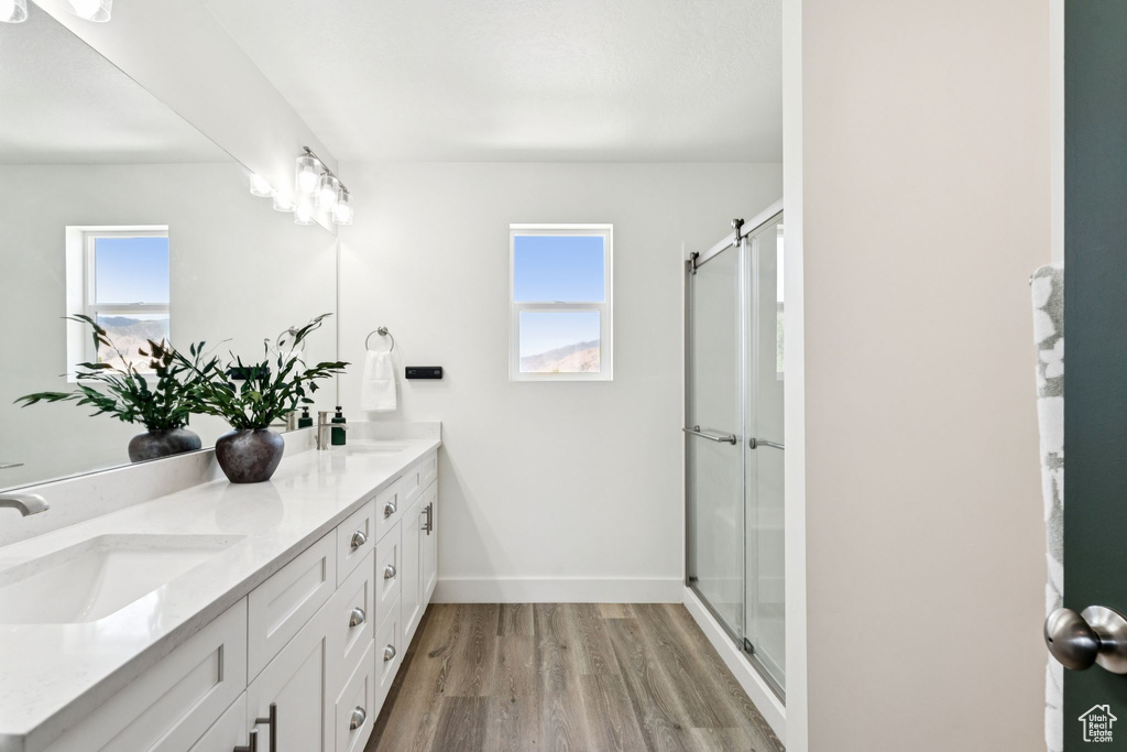 Bathroom featuring double vanity, wood finished floors, healthy amount of natural light, and a shower with shower door