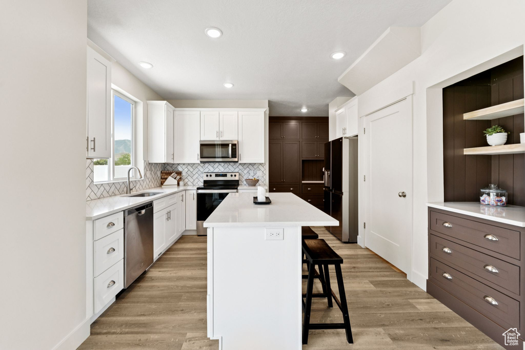 Kitchen with stainless steel appliances, a breakfast bar area, tasteful backsplash, white cabinetry, and light countertops