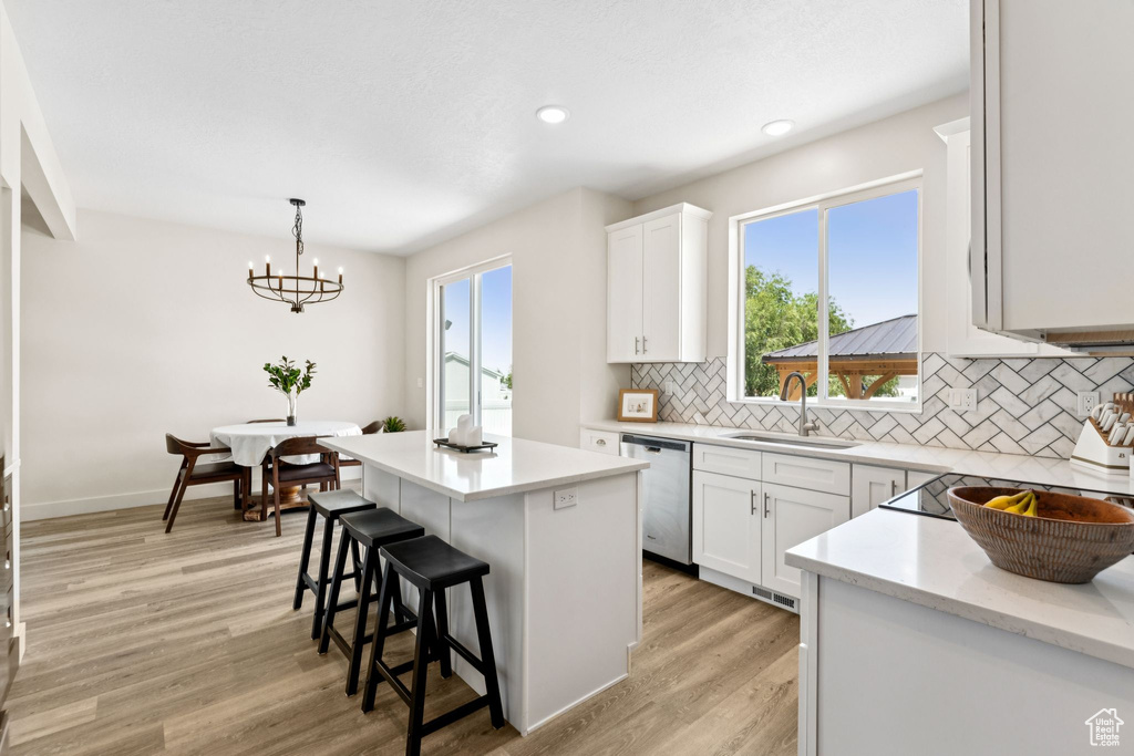 Kitchen with dishwasher, tasteful backsplash, light wood-style flooring, white cabinets, and a kitchen breakfast bar