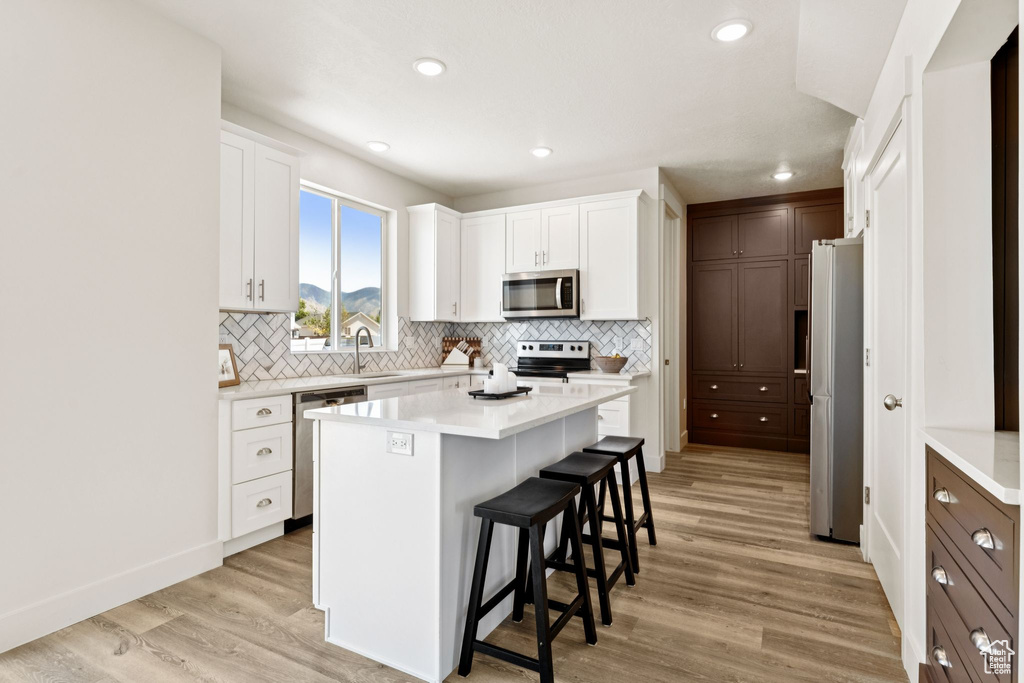 Kitchen featuring appliances with stainless steel finishes, a kitchen bar, decorative backsplash, light wood-type flooring, and white cabinets