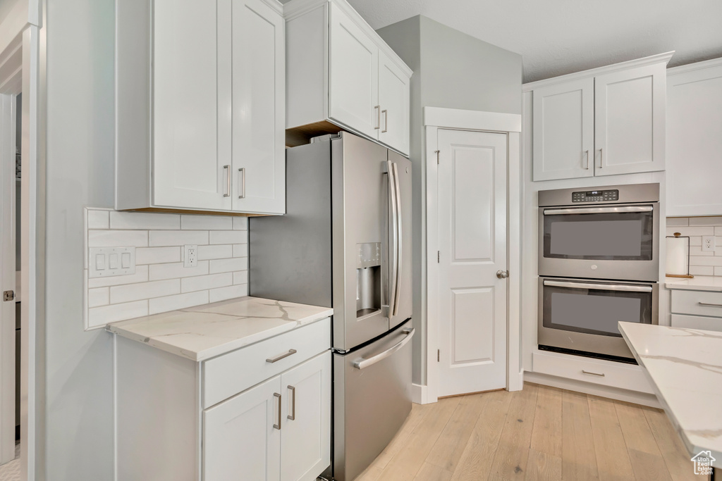 Kitchen with stainless steel appliances, light wood-style floors, white cabinets, and light stone counters